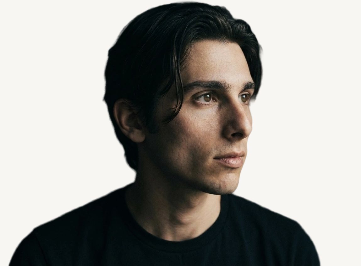 Tristan Colt, moody. Tristan Colt in three-quarter profile, half his face in shadow, looking off to the side, black t-shirt.